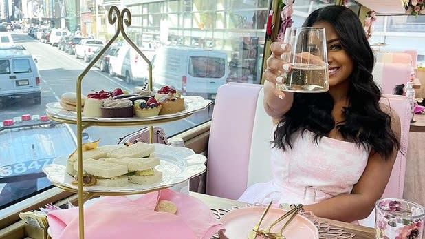A woman holding up a glass of sparkling wine next to a three-tiered stand of finger foods and pastries