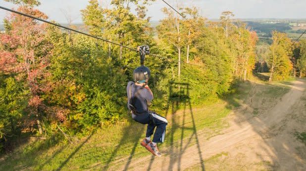 A child flies down a zipline over mountain views and fall foliage