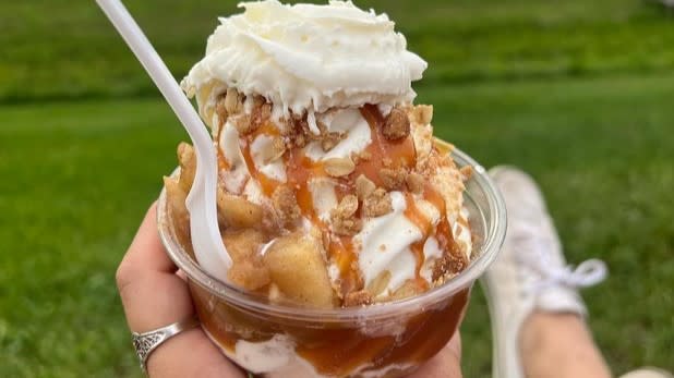 A hand holding a an apple crisp sundae (apple crisp, vanilla ice cream, caramel drizzle, crumble, and whipped cream)