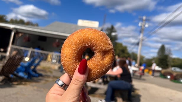 A person holding a cider donut in front of Tantillo's Farm Market