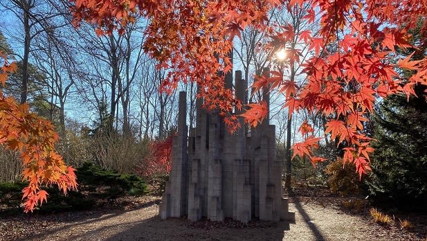 Sunshine peeks through bright red leaves surrounding a sculpture at Long Island's Longhouse Reserve