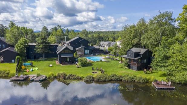 Aerial view of various dark grey buildings on a lakefront surrounding a blue outdoor swimming pool at Placid Bay Hotel