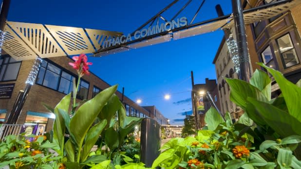 View of signage that says "Ithaca Commons" in front various storefronts at dusk.