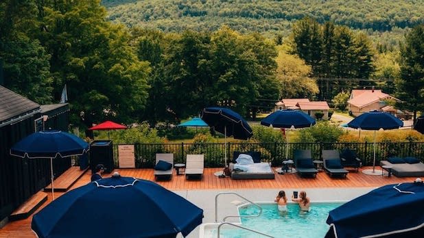 aerial view of two people relaxing in an in-ground pool surrounded by lounge chairs and mountain views