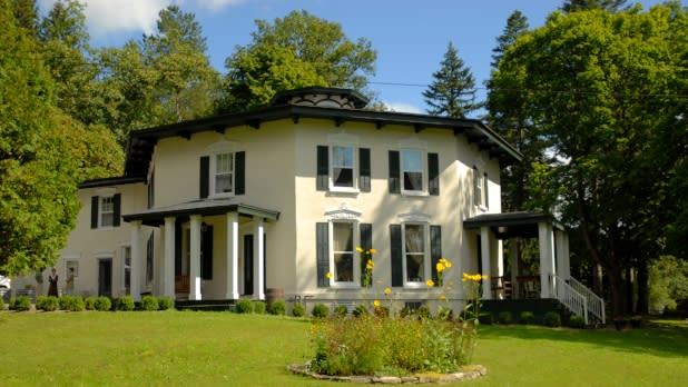 Exterior of a historic light yellow octagon-shaped house surrounded by green trees on a sunny day