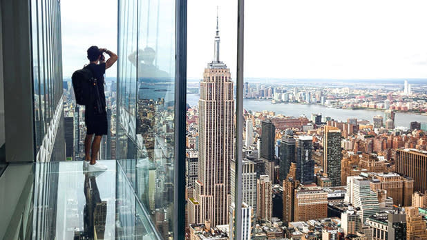 A man standing in the glass lookout at Summit One Vanderbilt taking a photo of the views across Manhattan and The Empire State Building
