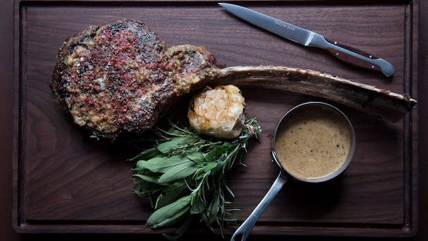 Meat, sauce, and greens on a wooden plate