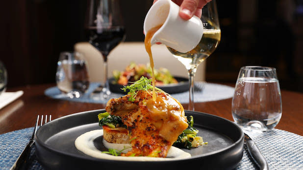A person pours gravy onto an entree alongside a glass of white wine at Panorama on Seven in Buffalo