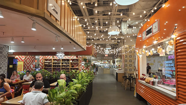 White string lights hang from the ceiling at a food market with restaurant seating
