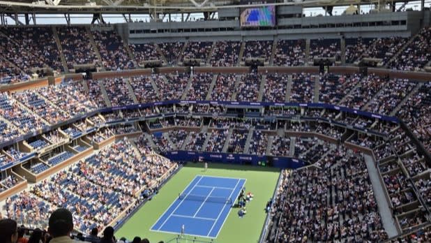 A view from above of a tennis court surrounded by a stadium of fans at the US Open
