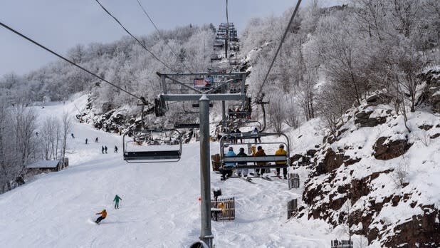 A ski lift bringing people up a snowy Hunter Mountain while skiers and snowboarders glide down the mountain