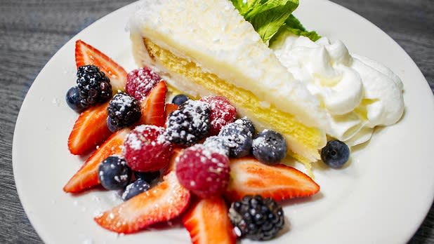 A slice of lemon cake with whipped cream and fresh berries covered in powdered sugar