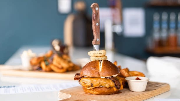 A gourmet cheeseburger on a wooden cutting board with fries and a knife speared through the top