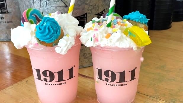 Pink-colored wine slushies topped with whipped cream, sprinkles and cookies in plastic cups labeled "1911 Established" on a counter at the Great New York State Fair.