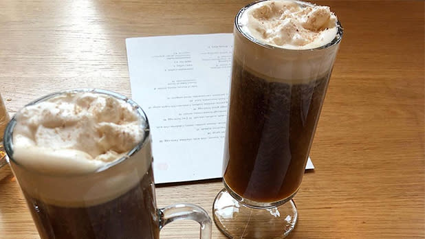 Two tall glasses filled with coffee, topped with whipped cream on a wooden table