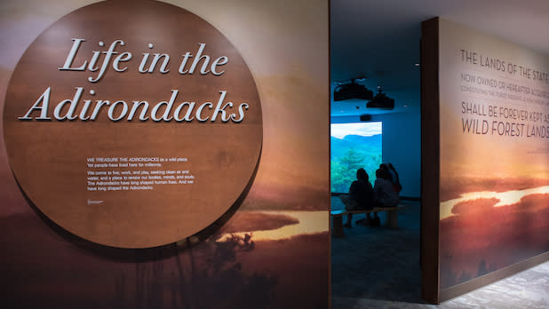an informational exhibit with that reads "Life in the Adirondacks" over top of a photo of an Adirondack sunset