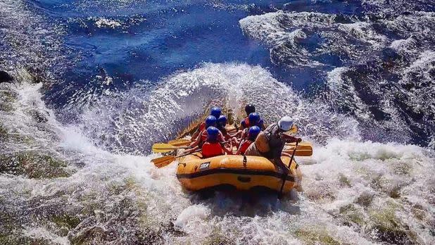 A group of people whitewater rafting through turbulent rapids on a yellow raft in Watertown