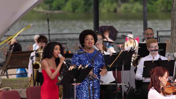Two women sing surrounded by a full orchestra on the water, a part of Water Music by the Albany Symphony
