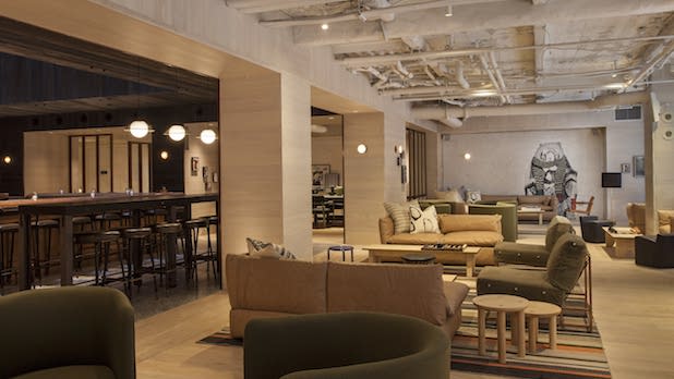 Interior of beige and grey couches and chair, and a bar with tall barstools at Bar Moxy in the Moxy NYC Times Square