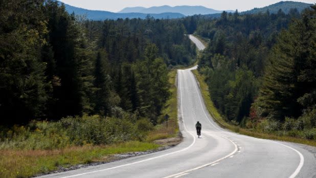 Lone cyclist on a long road in the Adirondacks in New York State.