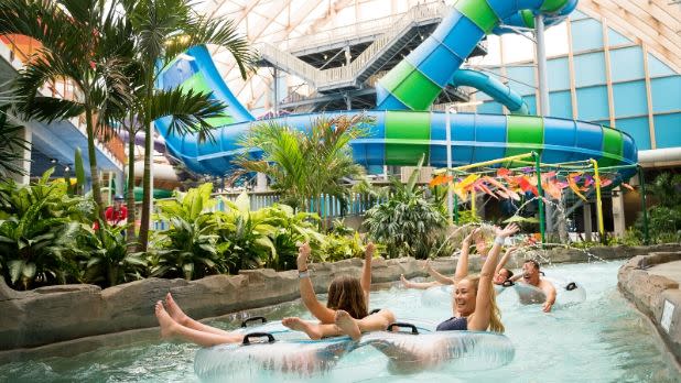 A group of people smiling as they lay in clear floating donuts along the water of the lazy river jungle-themed waterpark ride