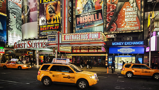 Yellow taxis driving by at night along Broadway with Broadway billboards all along Times Square