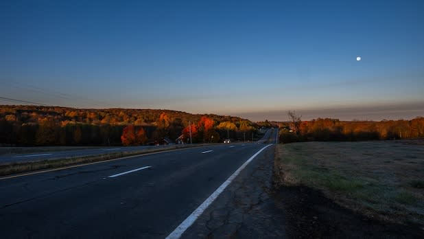 View driving in a car down Route 20 in Central NY at dusk toward rolling hills spotted with foliage