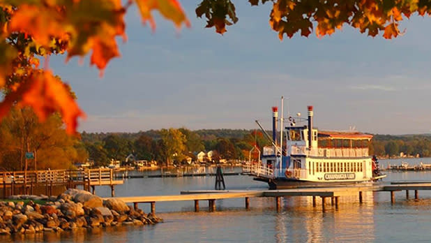 The Canandaigua Lady, a replica of a 19th-century double-decker paddlewheel boat, on the lake at sunset surrounded by fall foliage