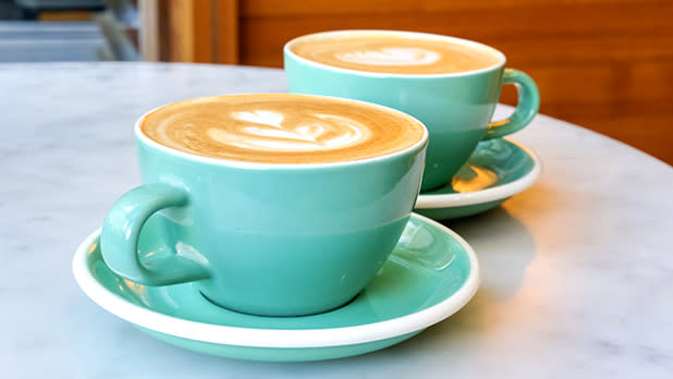 Two coffee cups filled with coffee and topped by foam milk