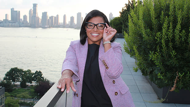 Debra Harris poses on a riverfront walkway in a lavender blazer