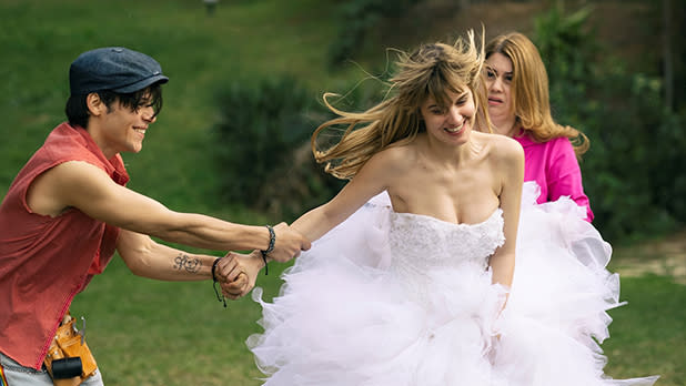 A woman in a white dress smiles as a man in a red vest grabs hold of her arm in a still from the film DODO