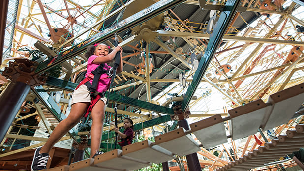 Young girl in a harness walking on a ropes course at Destiny USA.