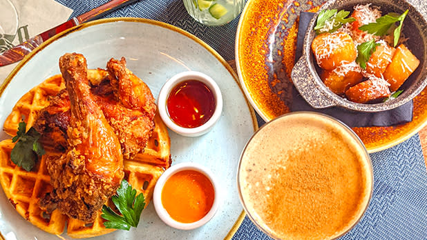 A plate of chicken and waffles, a side dish of vegetables and a cocktail at a restaurant in the theatre district