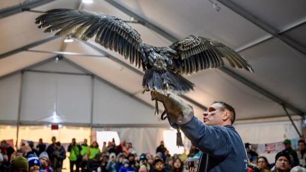 A man holds a large bird with outstretched wings inside a crowded tent at the Teatown Hudson River EagleFest