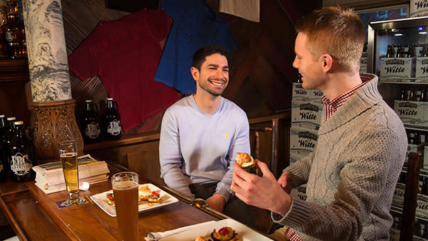Two men having conversation at a bar, plates of food and beer glasses in front of them