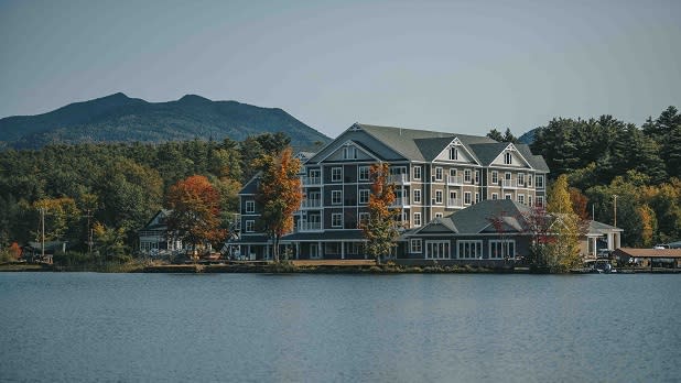 The stunning Saranac Waterfront Lodge surrounded by trees in the fall and mountains in the distance