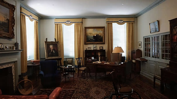 Intricately decorated room with a painting of FDR, a desk, and three windows with yellow curtains