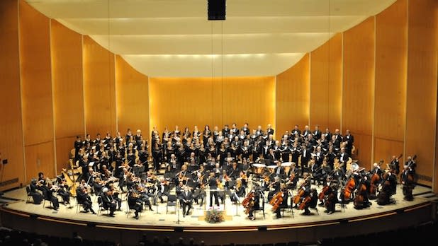 orchestra members dressed in all black perform in a large concert hall