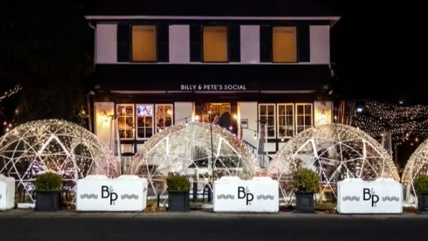 A group of igloos sitting in front of the black, white and yellow Billy Pete restaurant building at night