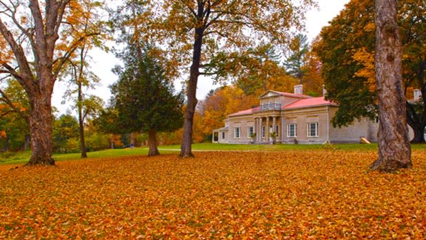 Orange leaves blanket the ground in front of the stately Hyde Hall mansion in Cooperstown