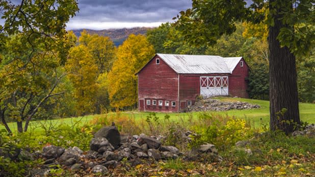 A red barn with a white roof nestled among the trees on Whites Farm Loop in the norther Catskills as trees start changing colors in fall