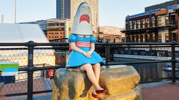 a girl in a dress with a shark head sitting on a rock at Canalside