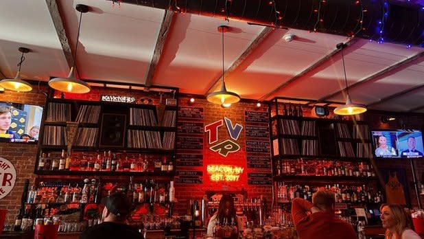 Shelves of records and bottles line the wall behind the bar, lit by a red neon sign that reads "TVR Beacon, NY Est. 2017"