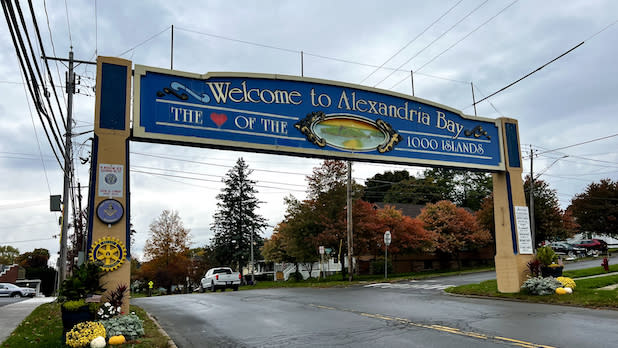 A blue sign arching over the street that reads "welcome to Alexandria Bay, The heart of the 1000 Islands"