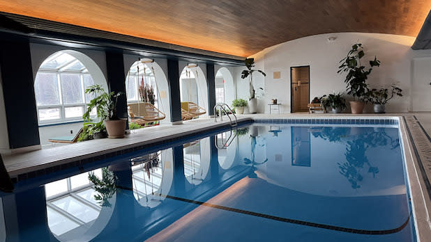 A blue indoor pool surrounded by windows that look out in a snowy Catskills landscape