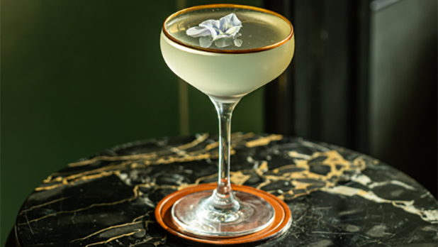 A cocktail in a martini glass topped with a floral garnish