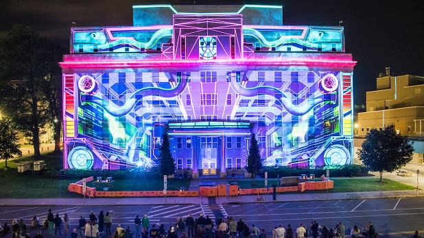 A colorful projection lights up a building at the LUMA Projection Arts Festival