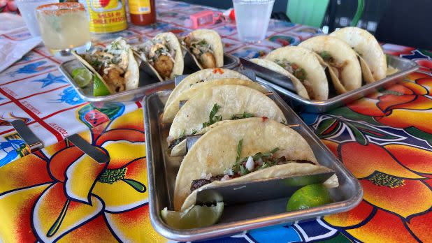 Three servings of tacos on a table with a colorful tablecloth.