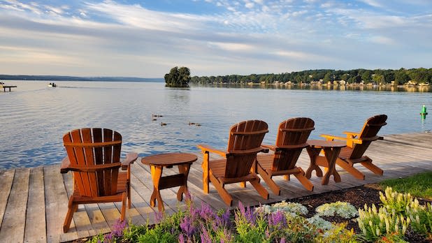 Four empty Adirondack chairs sit on a dock looking out at Canandaigua Lake