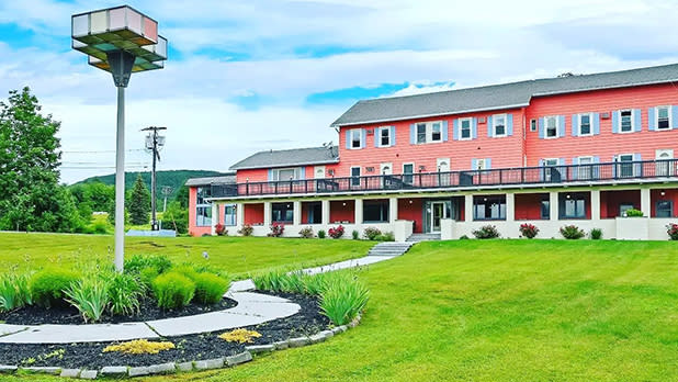 The peach exterior of Melour Resort and bright green grounds with views of the surrounding Catskills mountains and trees in summer